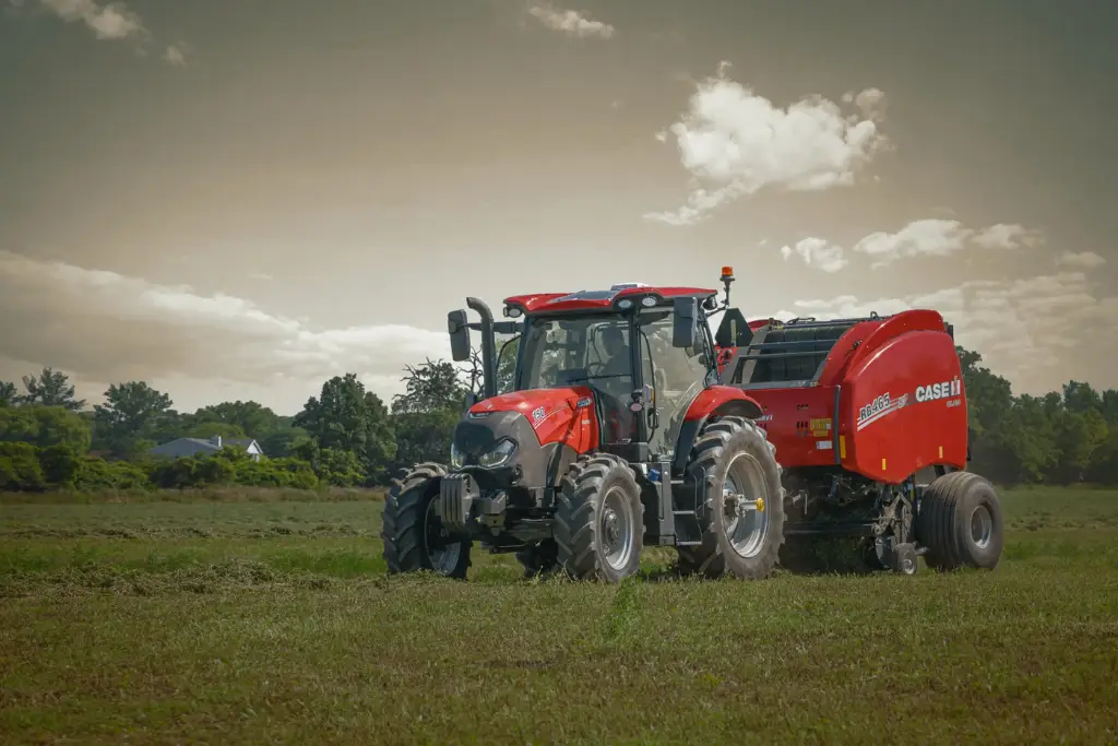 Case IH 220 CVT tractor operating a round baler attachment in a green pasture under a moody sky.