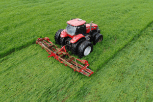 Overhead view of a red Case IH 340 tractor mowing a lush green field with a wide red implement.