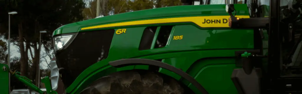 Close-up of a green John Deere 6R 185 tractor with yellow branding, photographed from the side.