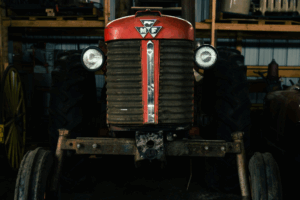 Frontal view of a vintage red Massey Ferguson tractor with MF emblem and headlights inside a workshop.