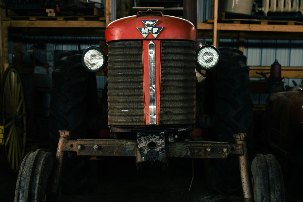 Frontal view of a vintage red Massey Ferguson tractor with MF emblem and headlights inside a workshop.