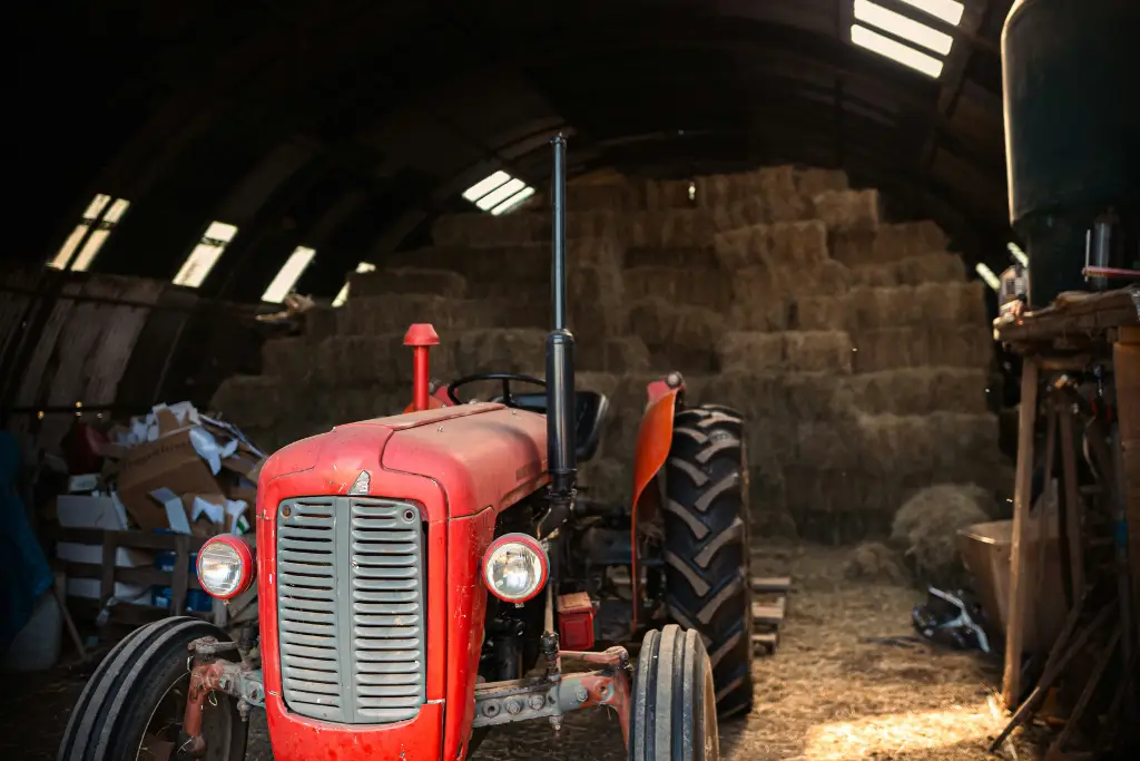 Vintage red Massey Ferguson tractor parked inside a barn filled with hay bales.