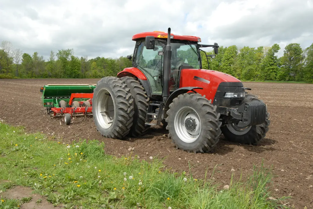 Red Massey Ferguson tractor pulling a green seeder across a plowed field under cloudy skies.