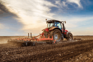 Massey Ferguson tractor cultivating a large farm field at sunset with dust rising behind it