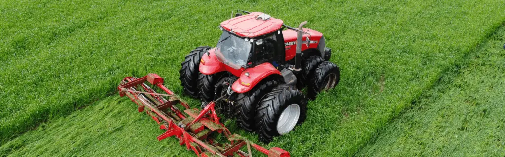 Overhead view of a red Case IH 340 tractor mowing a lush green field with a wide red implement.
